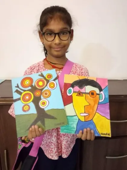 Two finished canvases, one proud artist. This student is happy to display her beautiful abstract tree and a colorful cubist-style portrait, showcasing the range of styles we explore.