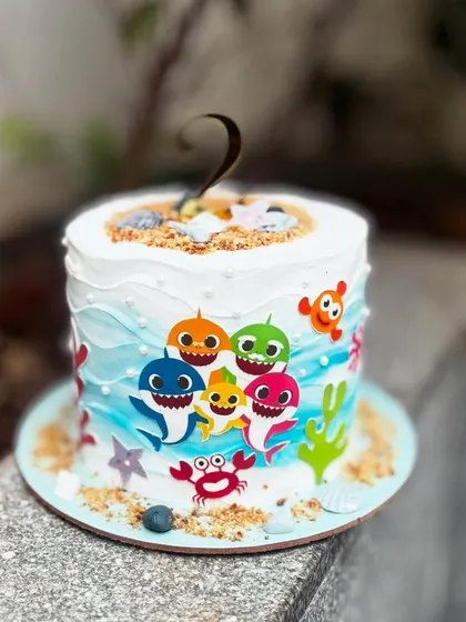 Here's a fun Baby Shark cake for a second birthday. I used edible character images, buttercream waves, and crushed biscuits for sand to create an underwater scene.