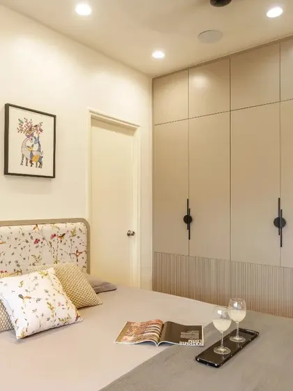 A wide shot of the bedroom, highlighting the beige wardrobe with black designer handles and fluted shutters.