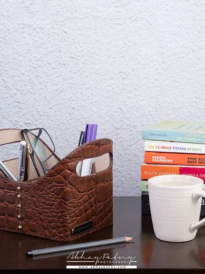 A lifestyle photograph of a premium leather desk organizer. Showing the product in a real-life context, filled with pens and glasses on a study table, helps customers imagine it in their own space.