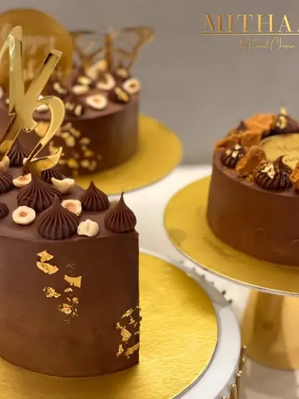 A trio of my rich chocolate cakes, each uniquely decorated. One is topped with Ferrero Rocher and hazelnuts, another with Biscoff cookies, showing the variety of custom designs I can create.
