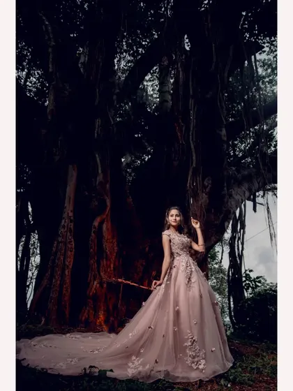 A wide shot capturing the grandeur of the pink wedding gown and its long train against the dramatic backdrop of an old tree.