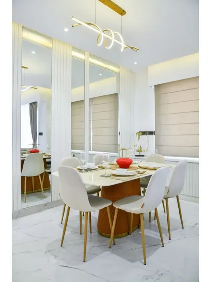 This elegant dining room uses full-length mirrors to create a sense of spaciousness and reflect light. The modern swirling light fixture and chairs with gold-toned legs add a touch of contemporary glamour.