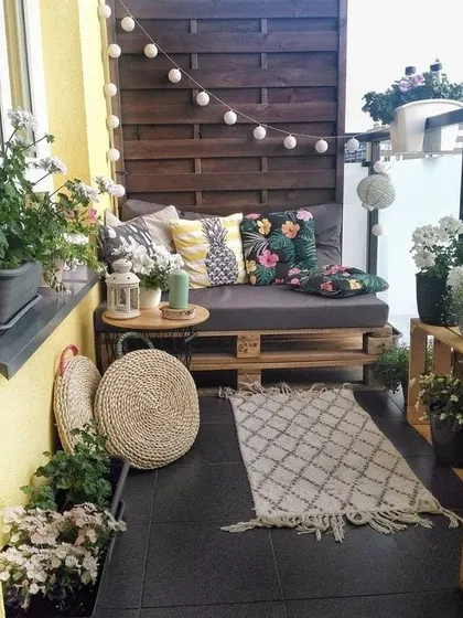 This cozy balcony uses a wooden privacy screen, string lights, and comfortable cushions to create an intimate and inviting outdoor nook, perfect for relaxing.
