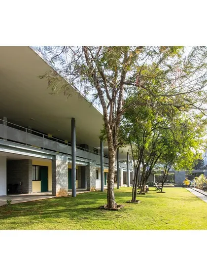 A long, shaded veranda provides circulation and a place for rest, looking out onto a green lawn.