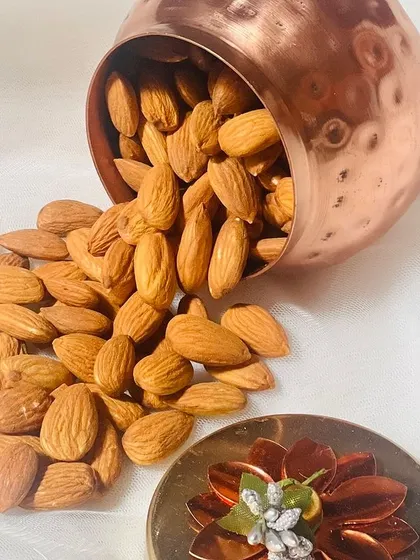 An artistic shot of almonds spilling from one of the hammered copper jars, highlighting the quality of the product.