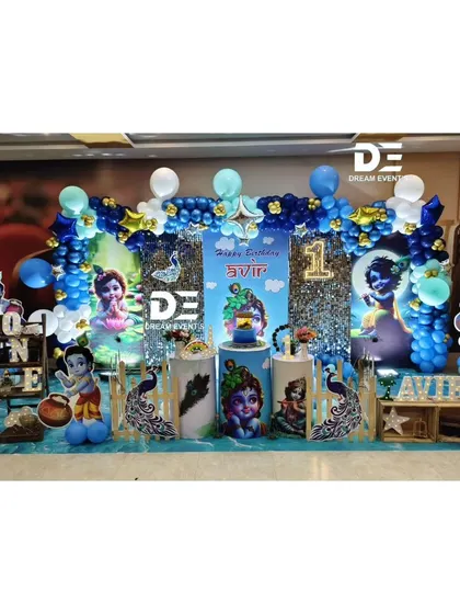 A divine Little Krishna theme for a first birthday party. The setup is decorated in shades of blue and silver, with peacock feather details and cutouts of the beloved character.