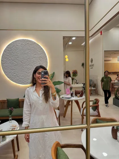 A mirror selfie from my June dump, wearing a simple white dress in a beautifully decorated cafe.