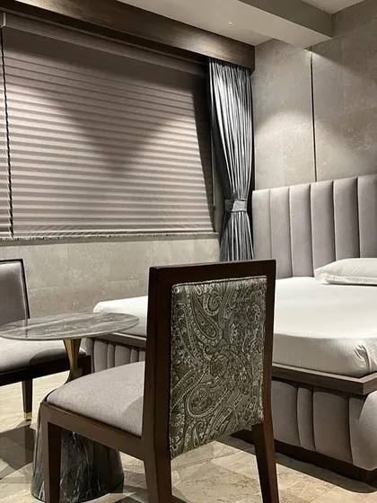 A quiet seating nook within a luxury bedroom in Juhu. The combination of a plush, channel-tufted bed, textured walls, and a chair with classic paisley upholstery creates a layered and sophisticated design.