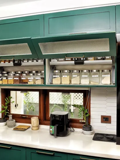 A beautifully organized kitchen with green cabinets and pull-down shelves for spices. This setup creates a perfect rhythm for cooking.