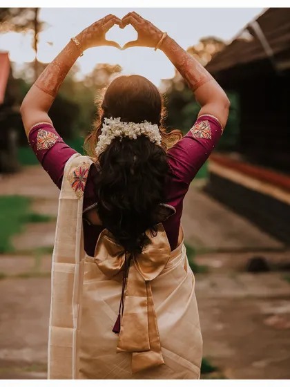 A creative shot of the bride from behind, making a heart shape with her hands against the setting sun.