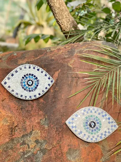 A pair of evil eye amulets, made from mosaic tiles, resting on a natural rock. These handmade pieces are perfect for adding a touch of color and protection to your indoor or outdoor spaces.