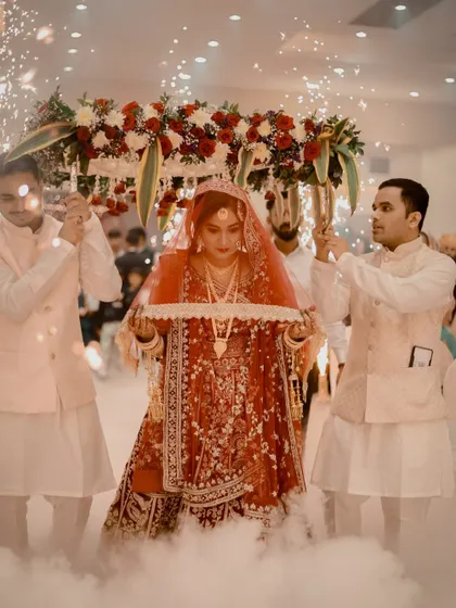 The bride's entry is a magical moment. I am so happy to see my bride looking absolutely radiant in a red lehenga, with makeup that glows even under the dramatic lighting and special effects of her grand entrance.