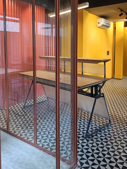 A detail of the material palette in a New Delhi office. The design juxtaposes a bold, patterned tile floor with a vibrant orange corrugated wall and a custom wood and steel desk, using color and texture to delineate different functional areas.