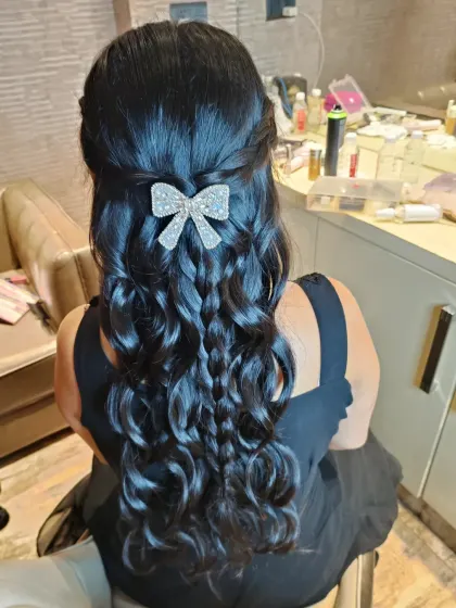 A playful half-up hairstyle featuring a combination of braids and curls, finished with a sparkling bow clip. This is a fun and youthful look for a bridesmaid or a pre-wedding party.