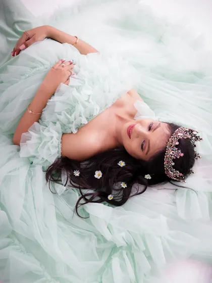 A dreamy, angelic portrait from above. The mom-to-be lies in a cloud of mint green tulle, wearing a crown and looking serene.