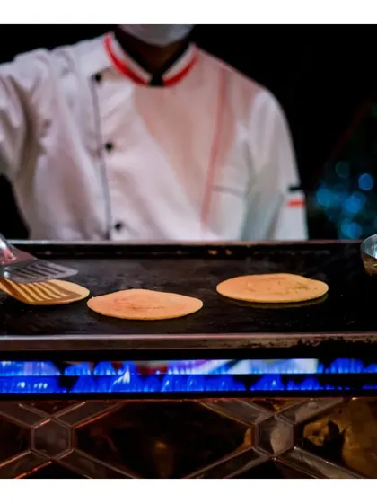 A chef prepares delicate cottage cheese chilas on a hot griddle. This live station offers a light and healthy Indian option, served hot and fresh.