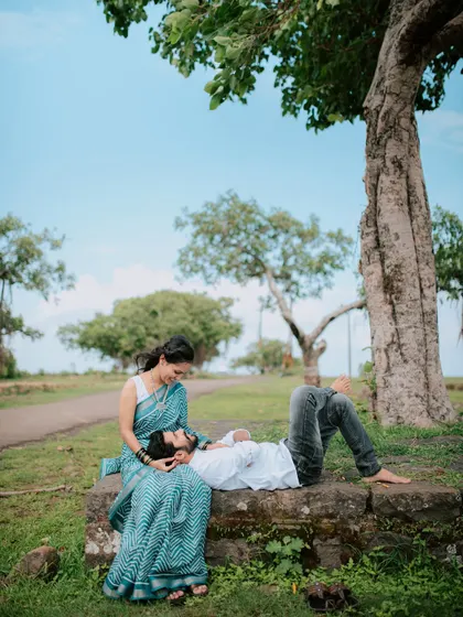 A romantic pre-wedding moment with the groom resting his head on the bride's lap under a tree.