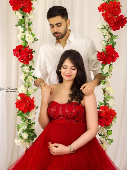 A romantic moment on the floral swing. The husband stands behind his wife, sharing a quiet moment of connection amidst the beautiful red and white flowers.