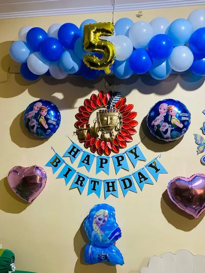 A simple yet charming "Frozen" themed birthday decoration for a 5th birthday. The setup includes a blue and white balloon garland, character foil balloons, and a "Happy Birthday" banner.