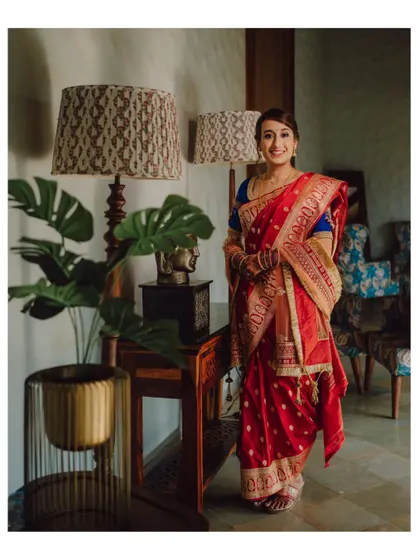A full-length portrait of a bride in her traditional sari, posing in a beautifully decorated room.