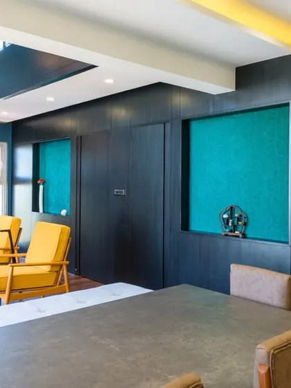An open-concept living area where the kitchen, dining, and lounge spaces flow seamlessly. The design uses color blocking with teal and dark wood to define different zones.