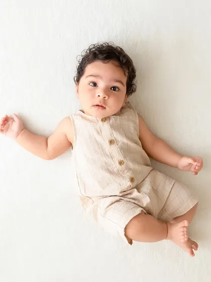 A baby lies on a simple white background, looking at the camera, showcasing a minimalist milestone portrait.