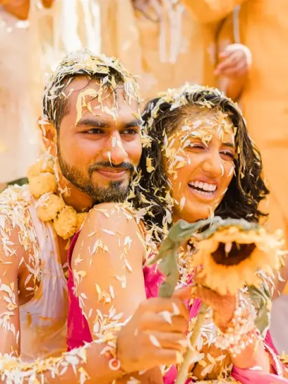 The couple, covered in petals and haldi, holds up a sunflower together. This photo is a beautiful summary of their joyful, vibrant, and love-filled ceremony.