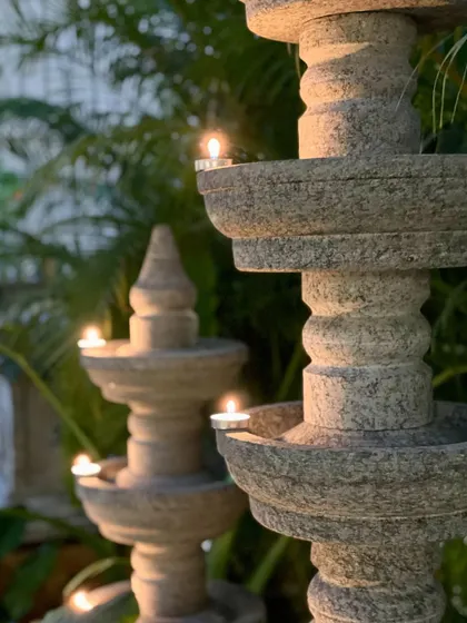 A close-up of our granite temple lamps lit with diyas, perfect for creating a warm and inviting glow in your garden during festivals.