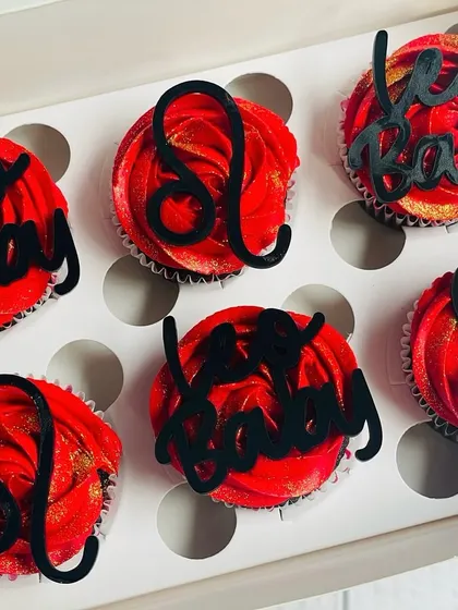 The complete box of Leo-themed cupcakes, showing the alternating "Leo Baby" and zodiac symbol toppers.