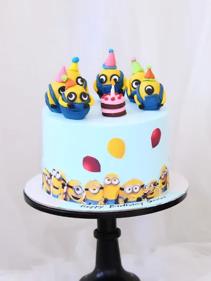 A playful Minions cake for a fan of the mischievous characters. This design features a border of printed Minions and is topped with handcrafted fondant Minions celebrating with a tiny cake.