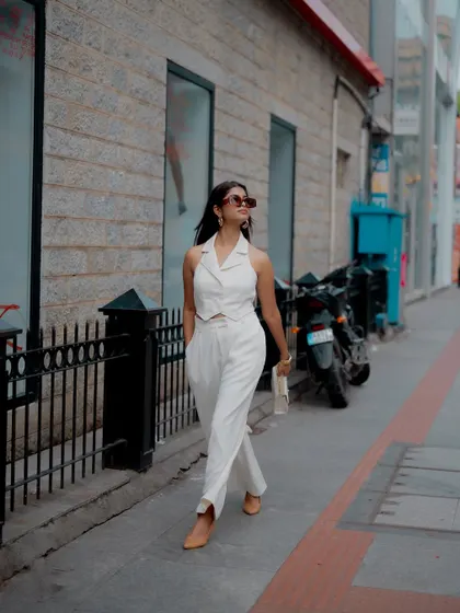 A full-length action shot of a model walking down a city street in a stylish white pantsuit. This type of "paparazzi" style shot is great for creating authentic and aspirational lifestyle content for a fashion blog or brand.