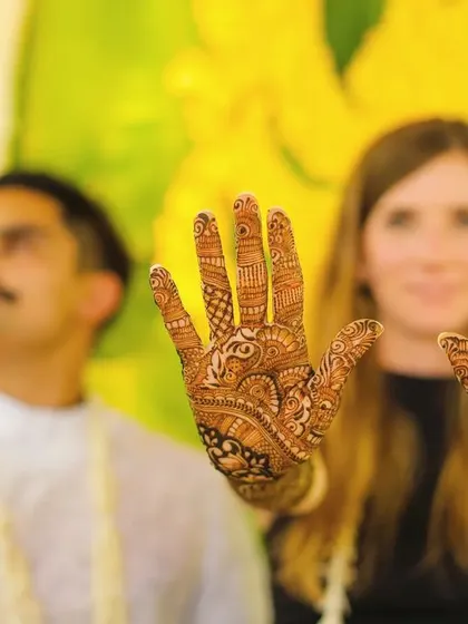 A close-up of a guest showing off her intricate Mehendi design. This photo highlights one of the central activities of the ceremony, with a vibrant yellow marigold backdrop.
