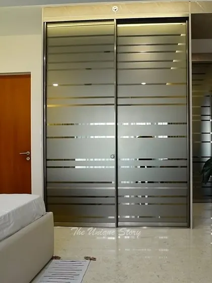 A close-up of a modern wardrobe with frosted glass sliding doors. The horizontal stripes on the glass add a graphic element while partially obscuring the contents, providing a clean and contemporary storage solution.