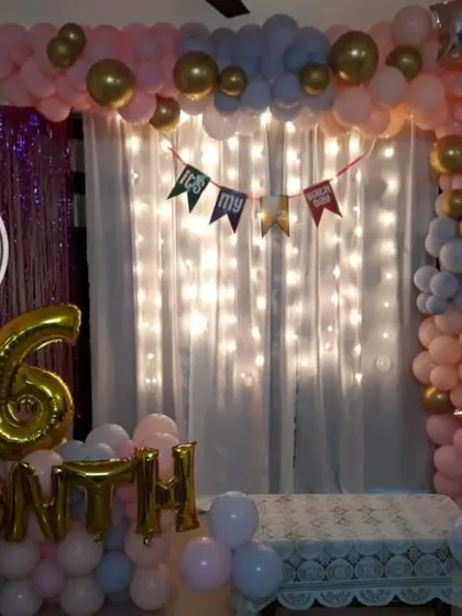 A sweet 6-month celebration setup at home, with a backdrop of fairy lights, a pink and blue balloon arch, and foil balloons marking the milestone.