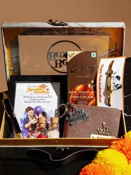A premium Rakhi hamper presented in a stylish trunk box. Inside, you'll find a personalized wallet, a 'Best Bro' keychain, a framed photo, a pen, a rakhi, and chocolate.