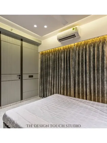 A view of the room showing the elegant curtains and the custom wardrobe design. The lighting is carefully planned to enhance the warm and inviting ambiance.