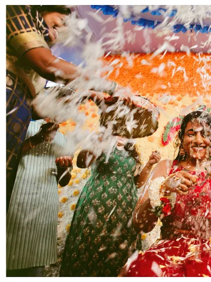 A dynamic shot from a wedding ritual, with guests showering the couple with flowers. The motion blur captures the energy of the celebration.