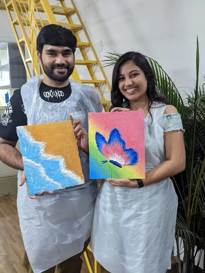 A couple showing off their finished texture paintings. One features a sandy beach, while the other is a colorful butterfly. It's a great activity to do together.