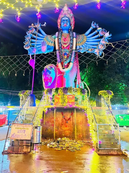 A massive deity statue at Amma Shakthi Peeta, illuminated with vibrant pink and blue lights for a dramatic nighttime effect.