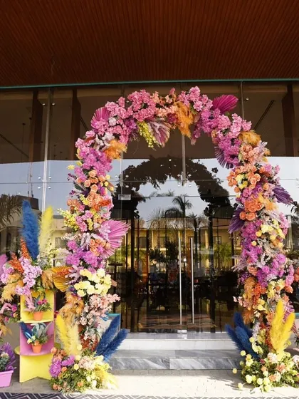 A magnificent floral arch in a riot of colors at the entrance of a building, setting the stage for a vibrant carnival-themed celebration.
