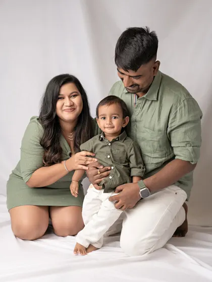 A classic family portrait against a simple white backdrop. The coordinated olive green outfits and their warm smiles create a clean, modern, and timeless image.