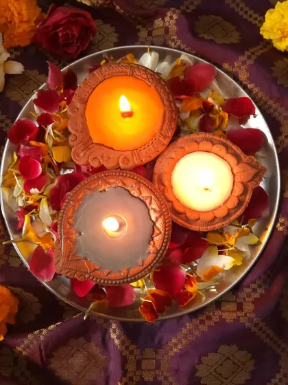 A trio of lit Diya Candles on a silver platter, surrounded by rose petals. This simple setup shows how beautifully they can be used to create a sacred prayer space.