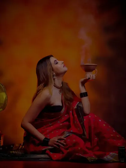 A dark and moody vintage-style portrait, with a model in a red saree holding a smoking incense bowl.