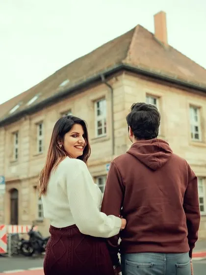 A playful "follow me" style shot on a European street. The woman looks back with a smile, inviting you into their romantic journey through the city.