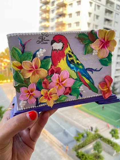 A full view of the macaw-themed utility stand, perfect for organizing makeup brushes or stationery. The vibrant colors of the bird and flowers are set against a soft lavender background.