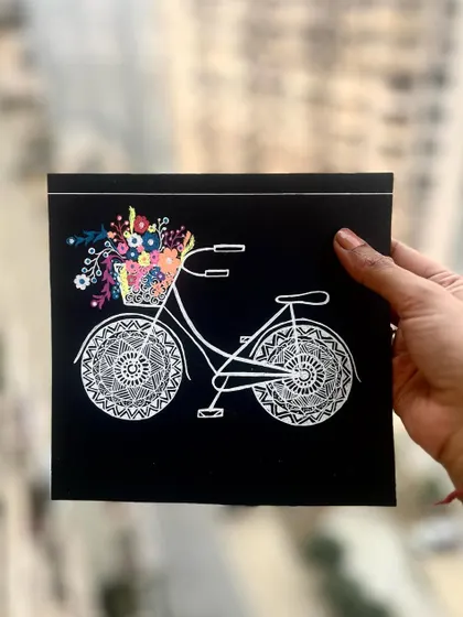 A classic bicycle with mandala-patterned wheels and a basket full of colorful flowers. This black and white piece with a pop of color is both elegant and charming.