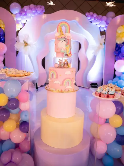 A birthday isn't complete without a cake. This multi-tiered unicorn cake was the centerpiece of the dessert table, surrounded by pastel balloons and rainbow decorations.