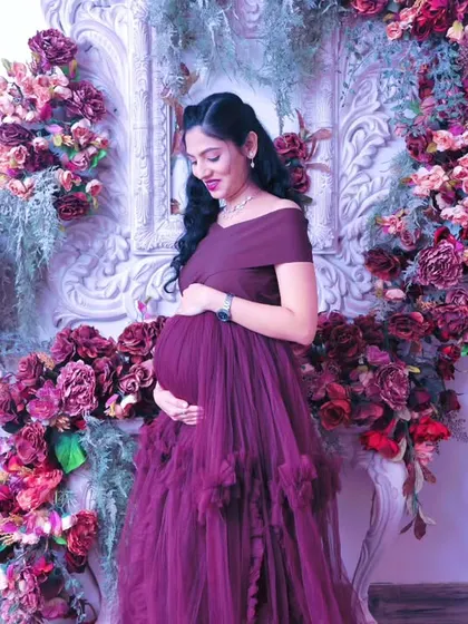 A candid, gentle moment of the mom-to-be looking down at her baby bump, surrounded by a beautiful frame of flowers.