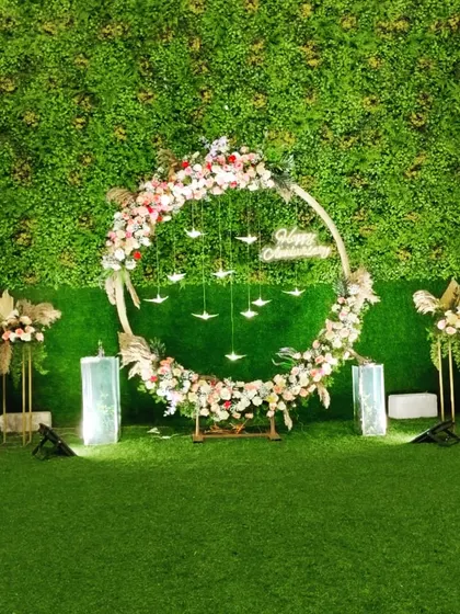 A simple and elegant floral decoration for a 25th-anniversary celebration. This outdoor setup features a floral ring against a greenery wall, creating a beautiful and natural photo backdrop.